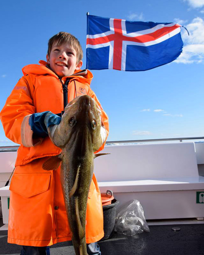 Boy holding a large fish on a boat.