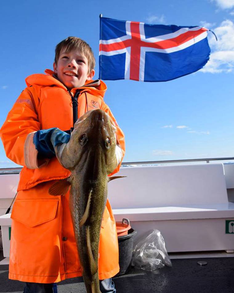 Boy in orange rain gear holding a caught fish